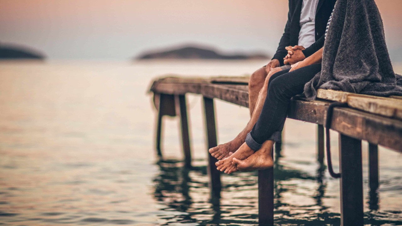 couple holding hands sitting on a dock over the water